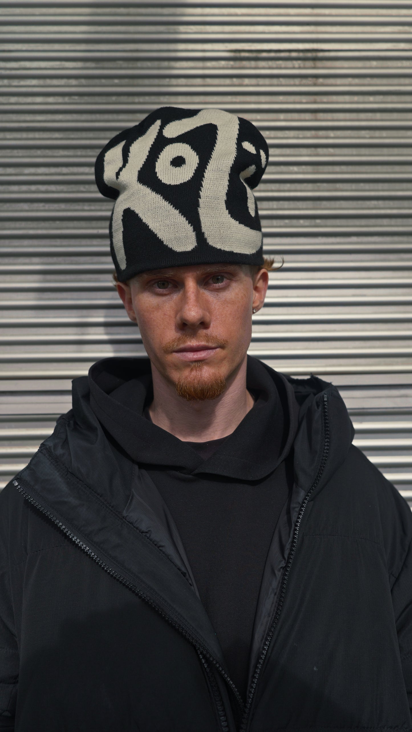 Person wearing a black and white patterned knit hat with the text "KOZI" against a metallic background
