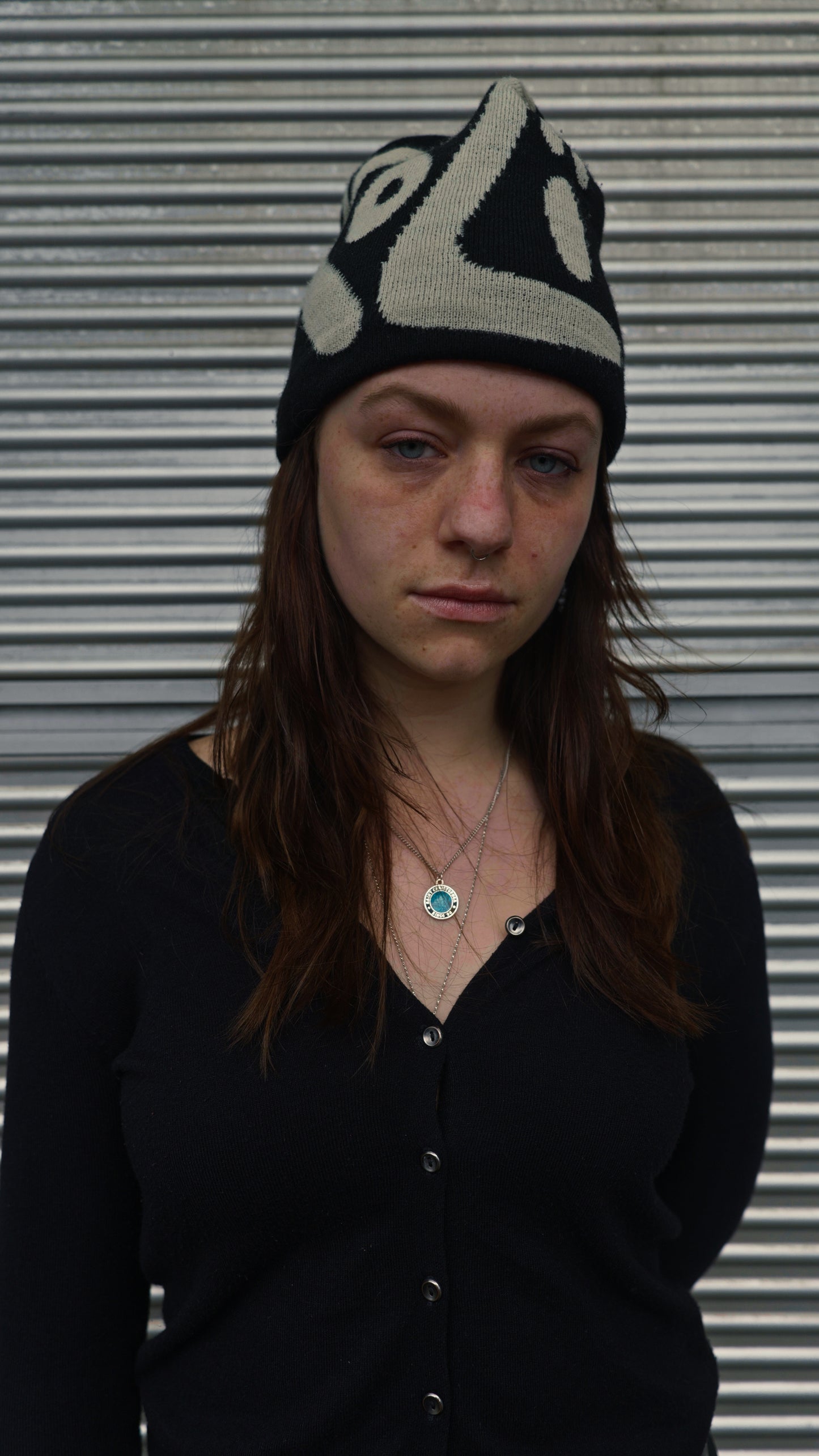 Person wearing a black and white patterned knit hat with the text "KOZI" against a metallic background