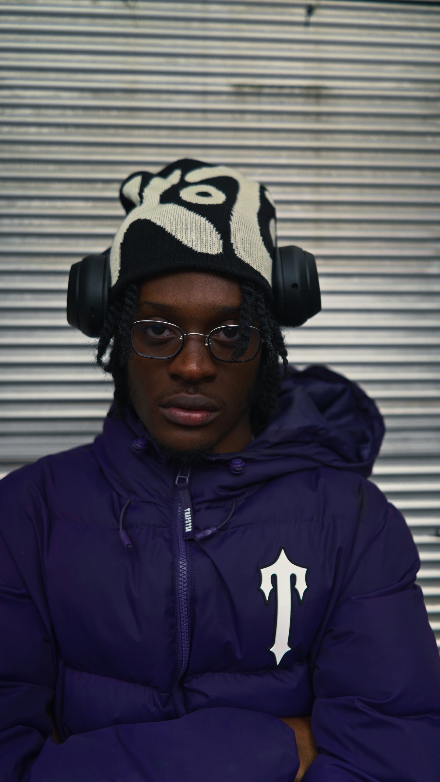 Person wearing a black and white patterned knit hat with the text "KOZI" against a metallic background