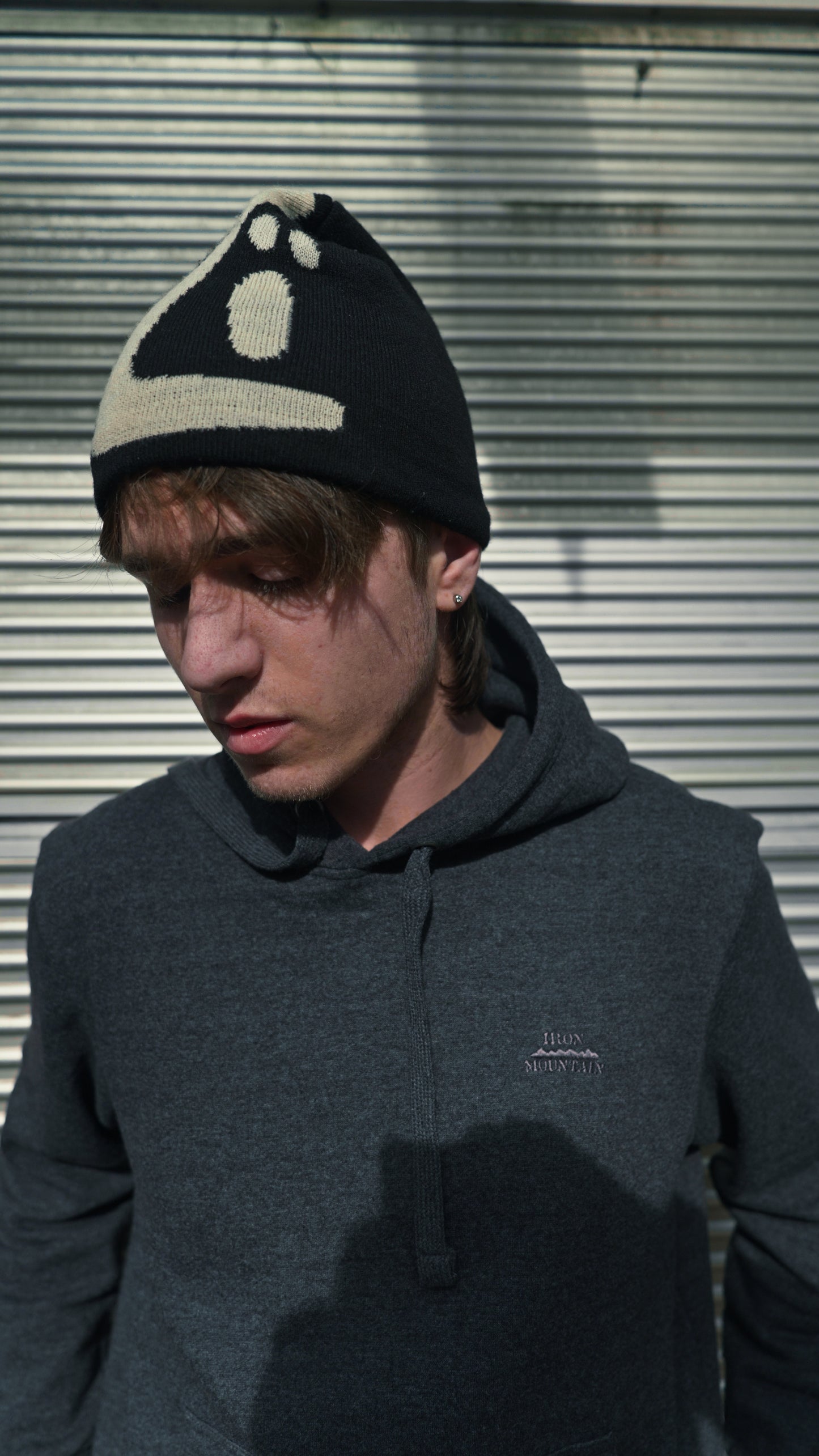 Person wearing a black and white patterned knit hat with the text "KOZI" against a metallic background